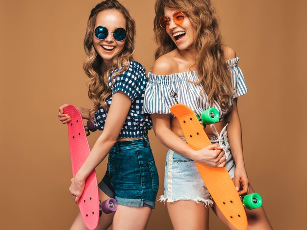 Deux jeunes filles élégantes souriantes avec des planches à roulettes de penny colorés. Modèles positifs s'amusant