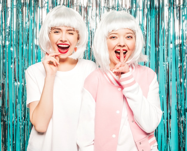 Deux Jeunes Filles Sexy Hipster Souriant En Perruques Blanches Et Lèvres Rouges. Belles Femmes En Vêtements D'été. Modèles Posant Sur Fond De Clinquant Brillant Argent En Studio.