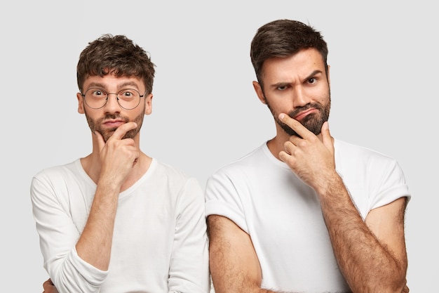 Deux jeunes hommes barbus tiennent le menton et regardent sérieusement la caméra, réfléchissent à la réalisation du projet