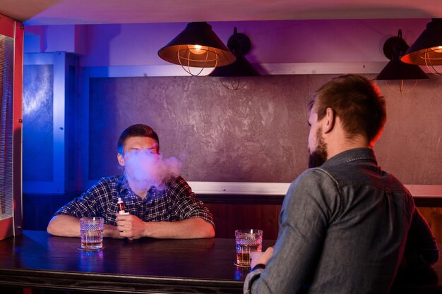 Deux jeunes hommes fument des cigarettes électroniques dans un vapebar. Boutique de vapotage