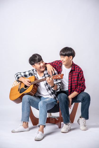 Deux jeunes hommes s'assirent sur une chaise et jouèrent de la guitare.