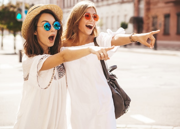 Deux jeunes mannequins hippies élégantes brune et blonde femmes modèles en journée ensoleillée d'été dans des vêtements de hipster blanc posant. Pointage sur les ventes en magasin