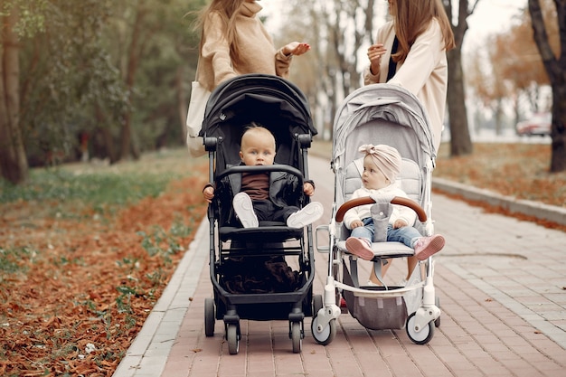 Photo gratuite deux jeunes mères marchant dans un parc en automne avec des calèches