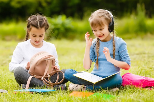 Deux jolies écolières multiculturelles assises sur une pelouse sous un arbre et lisant un livre ensemble