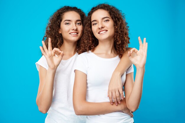 Deux jolies filles jumelles souriant, montrant bien sur le mur bleu