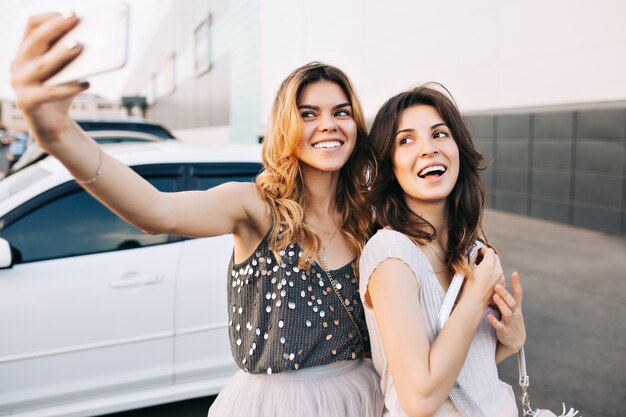 Deux jolies filles à la mode faisant selfie-portrait sur un parking.
