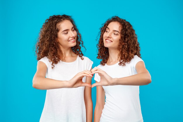 Deux jumeaux de femme montrant le cœur avec les mains sur le bleu.