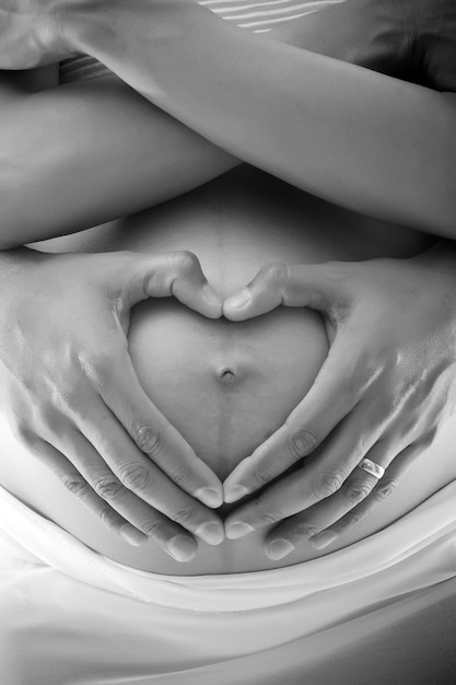 Photo gratuite deux mains en forme de cœur sur le ventre d'une mère enceinte