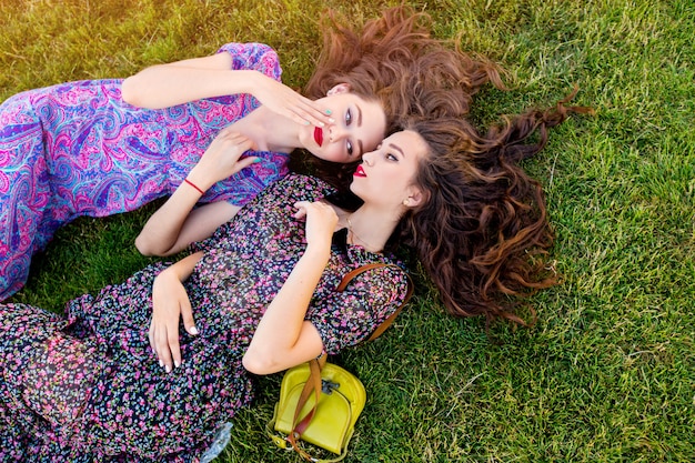 Deux meilleurs amis en robe boho colorée et cheveux bouclés portant sur l'herbe verte