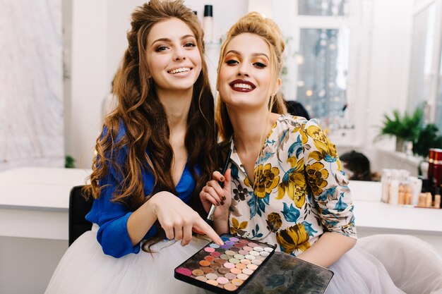 Deux modèles attrayants à la mode avec un maquillage élégant, une coiffure de luxe s'amusant ensemble dans un salon de coiffure