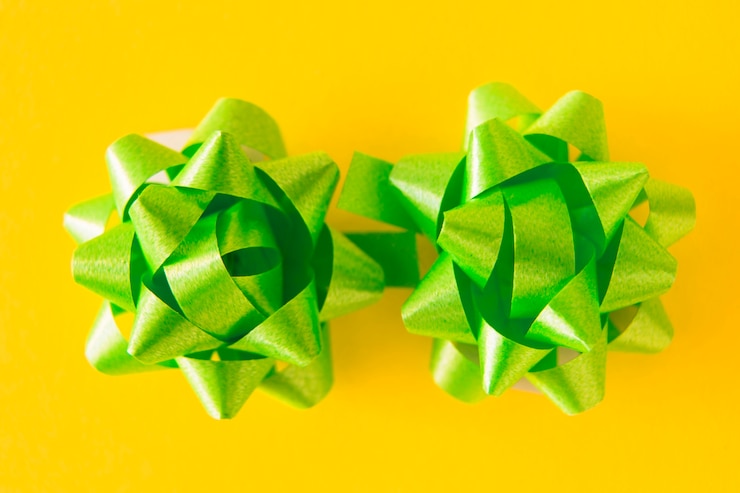 Photo gratuit deux noeuds de ruban de satin vert sur fond jaune