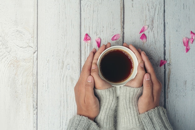 Deux personnes tenant une tasse de café dans les mains avec amour et chaleur sur la table en bois