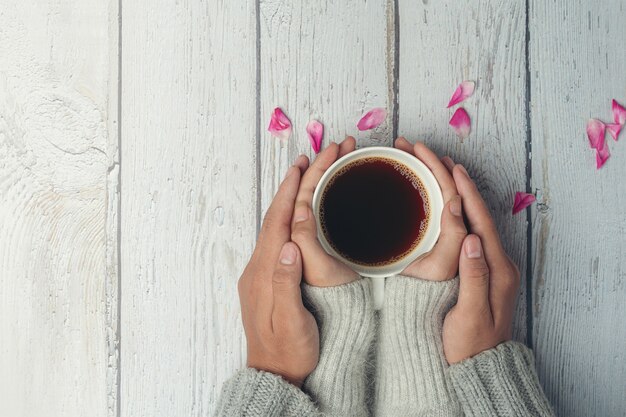 Deux personnes tenant une tasse de café dans les mains avec amour et chaleur sur la table en bois