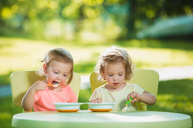 Deux petites filles assises à une table et manger ensemble contre la pelouse verte