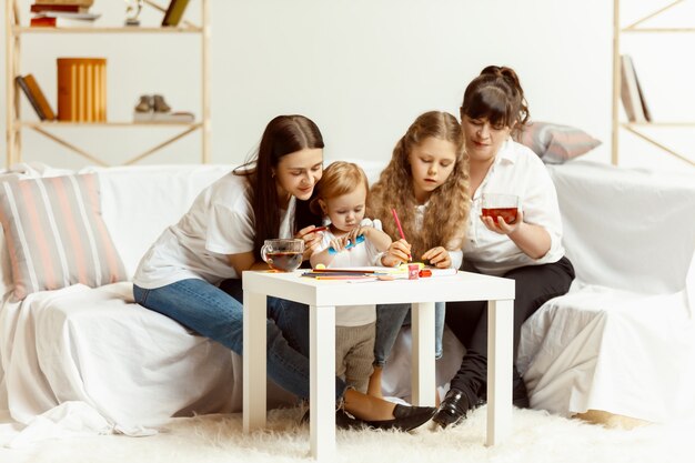 Deux petites filles leur jolie jeune mère et leur charmante grand-mère assise sur un canapé et passant du temps ensemble à la maison. Génération de femmes. Journée internationale de la femme. Bonne fête des mères.