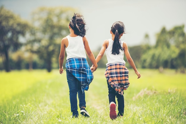 Photo gratuite deux petites filles tenant la main ensemble s'amuser dans le parc