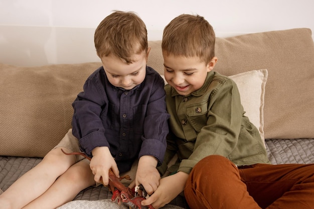 Deux petits garçons caucasiens mignons jouant avec des dinosaures à la maison. intérieur et vêtements aux couleurs de la terre naturelle. environnement cosy. enfants s'amusant avec des jouets, deux amis.