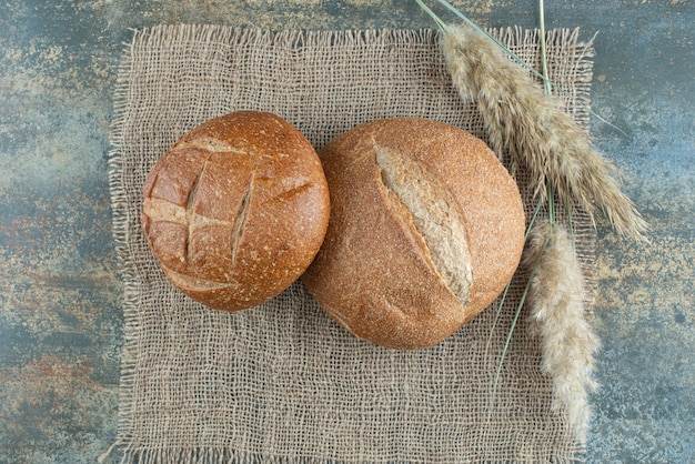 Deux petits pains brun frais avec du blé sur un sac
