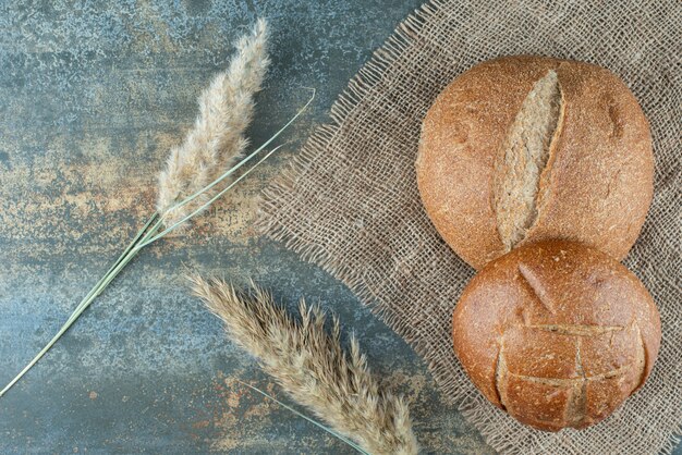 Deux petits pains brun frais avec du blé sur un sac