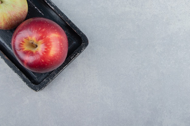 Deux pommes fraîches sur une planche à découper noire.