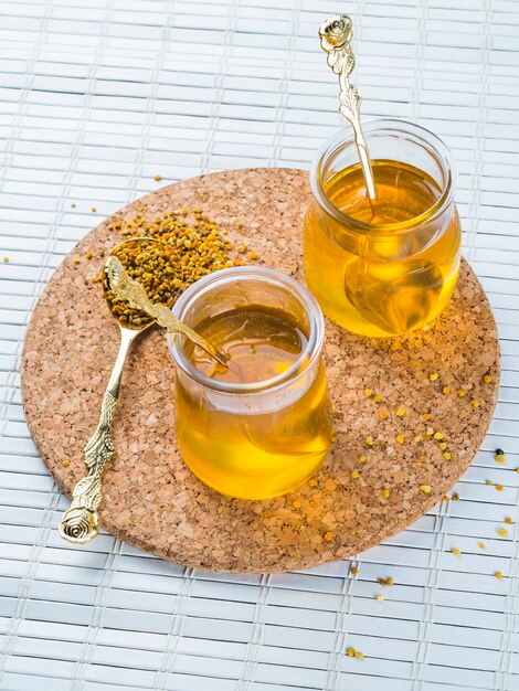 Deux pots de miel avec du pollen d&#39;abeille sur des montagnes russes circulaires sur un napperon