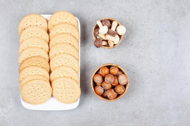 Deux rangées de biscuits sur un plateau à côté de petits bols de champignons au chocolat et de noisettes sur fond de marbre. Photo de haute qualité