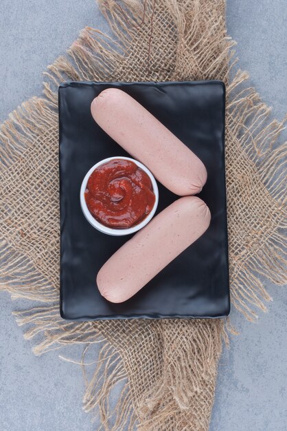 Deux saucisses bouillies fraîches avec du ketchup sur plaque noire.