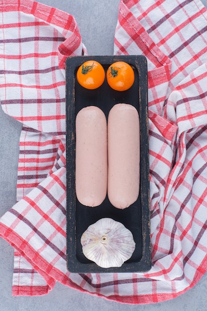 Photo gratuite deux saucisses bouillies fraîches avec tomate cerise et ail sur plaque noire.