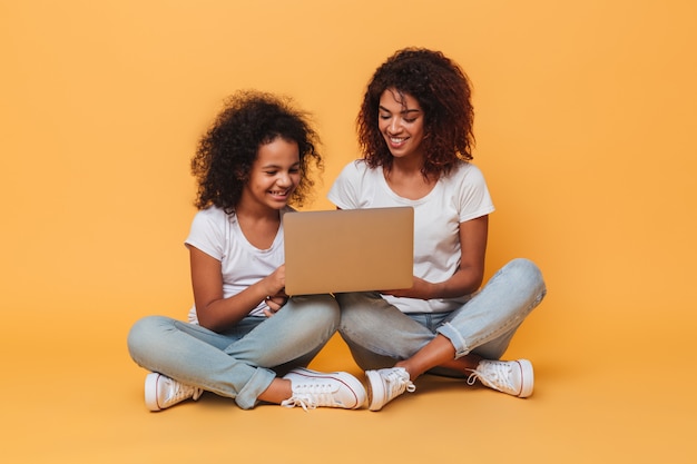 Deux sœurs afro-américaines souriantes à l'aide d'un ordinateur portable tout en étant assis