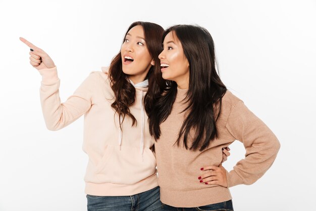 Deux soeurs asiatiques assez heureux mesdames étreignant pointant.