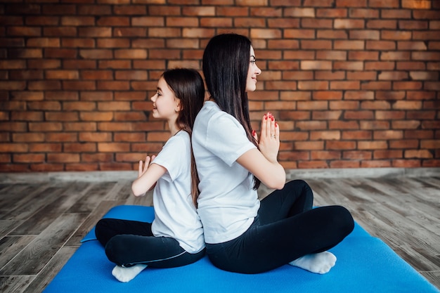 Deux sœurs assises dos à dos au gymnase et pratiquant le yoga.