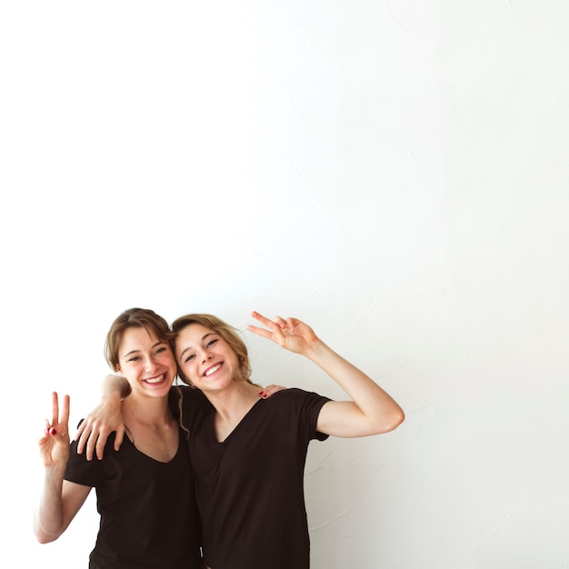 Photo gratuite deux soeurs faisant signe de victoire sur fond blanc