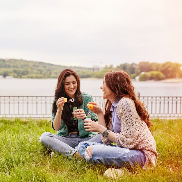 Deux soeurs gaies assis sur l'herbe et soufflant des bulles