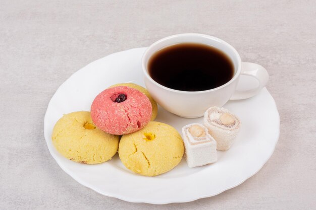 Deux sortes de biscuits, délices et tasse de thé sur une assiette blanche.