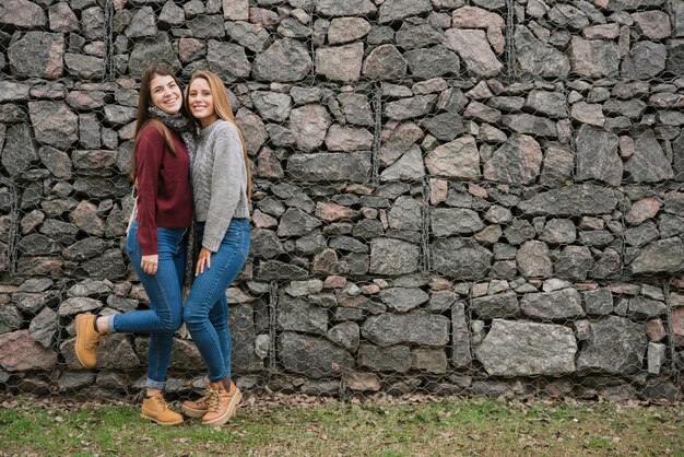 Deux, sourire, jeunes femmes, devant, mur pierre