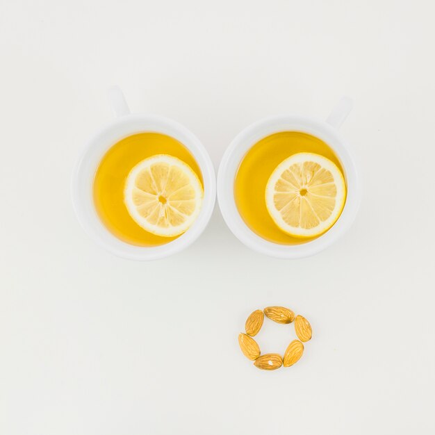 Deux tasse de thé au gingembre avec une tranche de citron et amandes isolées sur fond blanc