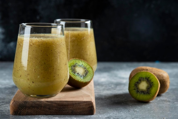 Deux tasses en verre de délicieux jus de kiwi sur planche de bois.