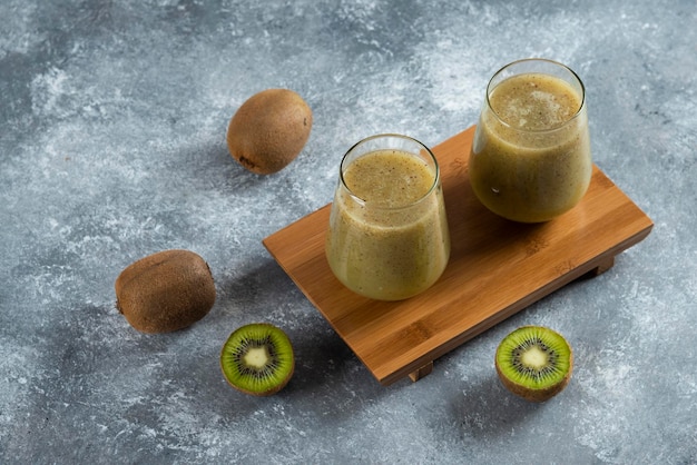 Deux tasses en verre de délicieux jus de kiwi sur planche de bois.