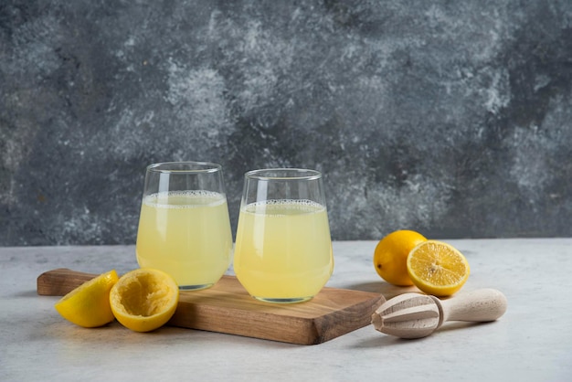 Deux tasses en verre de jus de citron frais sur une planche de bois.