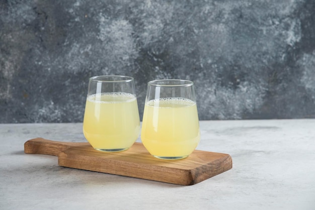 Deux tasses en verre de jus de citron sur une planche de bois.