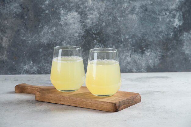 Deux tasses en verre de jus de citron sur une planche de bois.