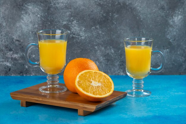Deux tasses en verre de jus d'orange sur planche de bois.