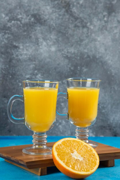 Deux tasses en verre de jus d'orange sur planche de bois.