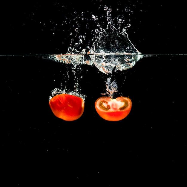 Deux tomates rouges fraîches coupées en deux tombant dans l&#39;eau