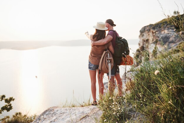Deux touristes hommes et femmes avec des sacs à dos se tiennent au sommet de la falaise et profitent du lever du soleil.