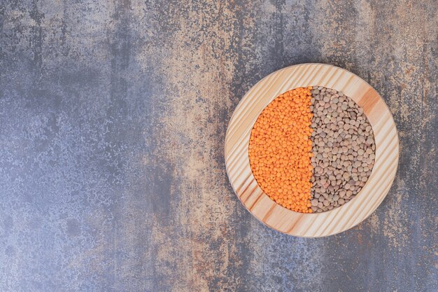 Deux types de haricots crus et de lentilles dans une assiette en bois.