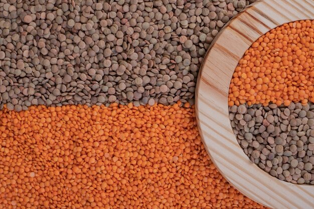 Deux types de haricots crus et de lentilles dans une assiette en bois.