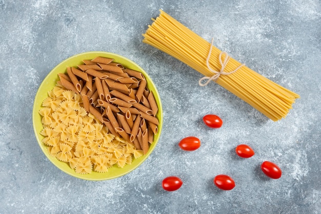 Deux types de pâtes crues sur assiette avec des tomates et des spaghettis.