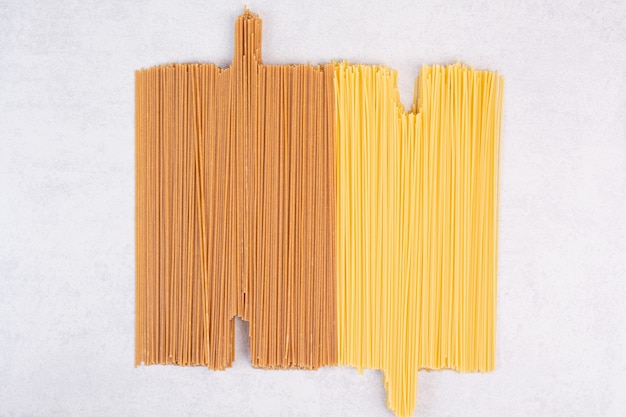 Deux types de pâtes spaghetti crues sur une surface blanche