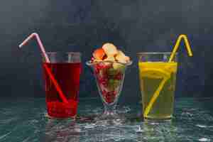Photo gratuite deux verre de cocktails avec des pailles et un verre de fruits mélangés sur une table en marbre.